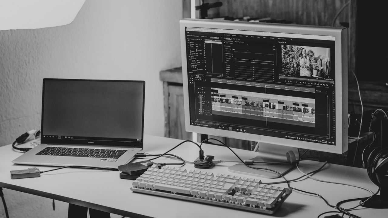 Video editing timeline open on a monitor next to a laptop — a typical outsourced editing setup